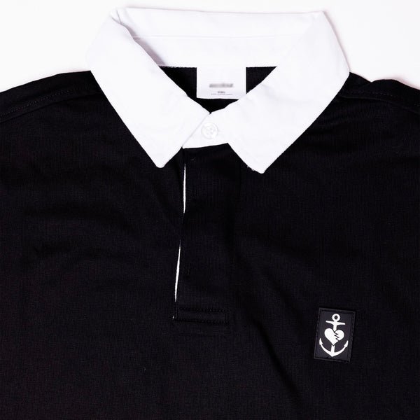 close up of the white patch sewn on the chest of the black pullover hoodie of an anchor and heart
