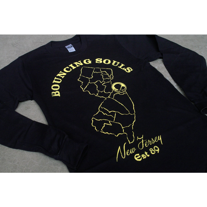  Image of a black long sleeve lying against a grey background. The shirt says Bouncing souls in yellow text in a semi circle shape, and below that is a photo of new jersey, with the bouncing souls abstract logo on it. Below that it says New Jersey, est 89 in yellow.